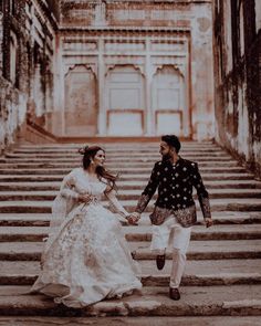 a man and woman holding hands while walking up some steps in front of an old building