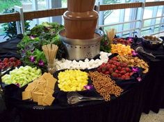 a chocolate fountain surrounded by fruits and other foods on a table with black cloths