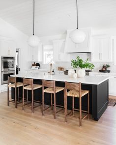 a kitchen with white cabinets and black island in the center is surrounded by wooden stools