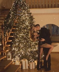 a man and woman kissing in front of a christmas tree