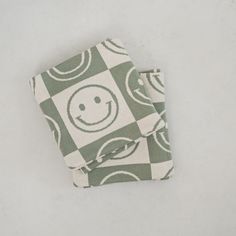 a green and white checkered towel with a smiley face on the front, sitting on a gray surface