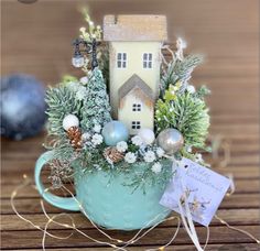 a small house in a teacup filled with greenery and christmas decorations on a wooden table