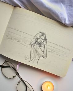 an open book with a drawing of a woman on it next to glasses and a candle