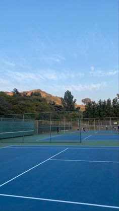 two people playing tennis on a blue court with mountains in the backgrouds