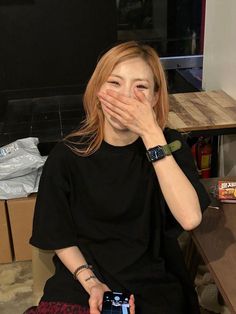 a woman covering her mouth while sitting on the floor with a cell phone in front of her