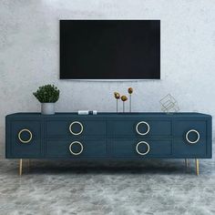 a tv is mounted on the wall next to a blue dresser with gold handles and two potted plants