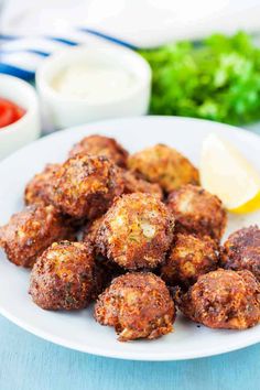 some meatballs are on a white plate with lemon wedges and ketchup