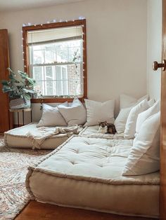 a living room filled with lots of white furniture and pillows on top of a wooden floor