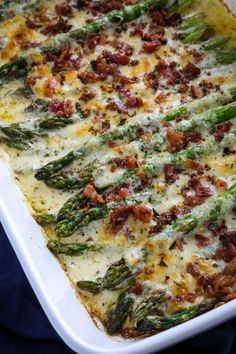 a casserole dish with asparagus, bacon and cheese in it on a blue cloth