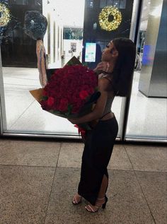 a woman holding a bouquet of red roses in front of a store window with the doors open