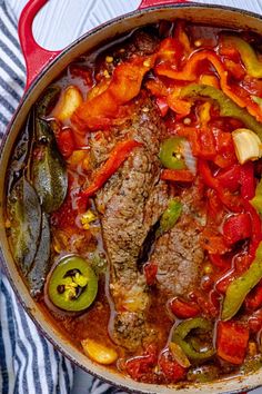 a pot filled with meat and vegetables on top of a striped table cloth next to a fork