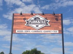 a large sign for plank and tile in front of a blue sky with white clouds