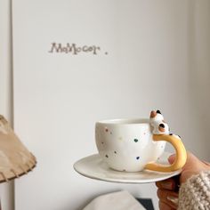 a person holding a coffee cup and saucer with a cow on the rim, in front of a white wall