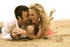 a man and woman laying in the sand on top of each other with their arms around each other