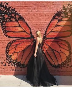 a woman standing in front of a brick wall with a large butterfly painted on it