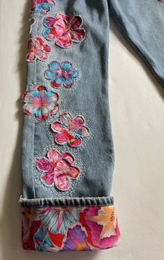 an old pair of jeans with embroidered flowers on the bottom and sides, sitting on a white surface