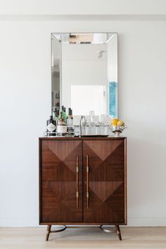 a wooden cabinet with a mirror on top of it next to a white wall and hardwood floor