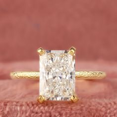 a yellow gold engagement ring with a princess cut diamond in the center on a pink background