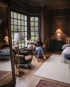 a woman sitting on a chair in a room with lots of windows and rugs