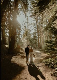 a bride and groom walking down a dirt path in the woods with sun shining through the trees