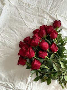 a bunch of red roses laying on top of a white sheeted bed spread with green leaves