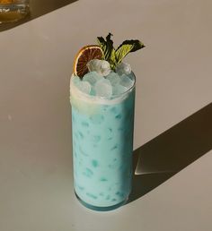 a blue drink with ice, orange slice and mint on the rim sitting on a table