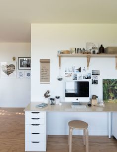 a white desk topped with a computer monitor next to a wooden floor covered in pictures