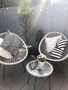 two wicker chairs sitting on top of a wooden deck next to a table with flowers