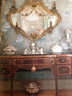 an antique dresser and mirror in front of a wallpapered wall with floral designs