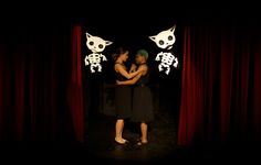 two women standing in front of red curtains with skeleton decorations on the wall behind them