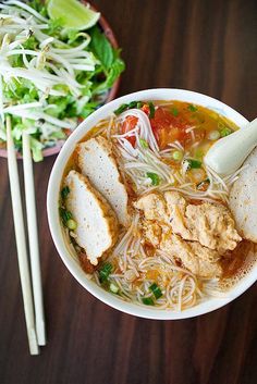 two bowls filled with noodles, meat and veggies next to chopsticks