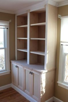 an empty living room with built in bookshelves and cabinets on the wall next to two windows