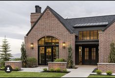 a brick house with large windows and black trim on the front door is shown at dusk