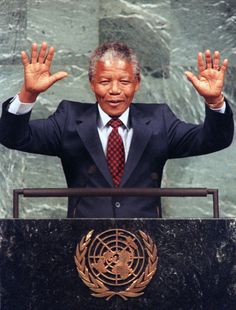 a man in a suit and tie standing at a podium with his hands raised up