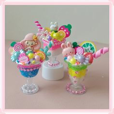 two small plastic cups filled with candy and candies on top of a pink table