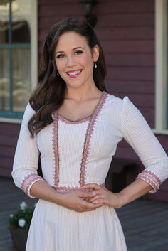 a woman standing in front of a house wearing a white dress with pink trims