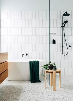 a bath tub sitting next to a wooden table in a white tiled bathroom with green towels on it