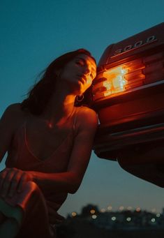 a woman sitting on the hood of a car with her back turned to the camera