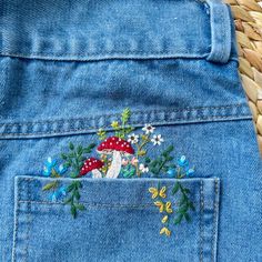 the back pocket of a pair of blue jeans with embroidered mushrooms and flowers on them