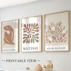 three framed art prints hang on the wall above a table with vases and books