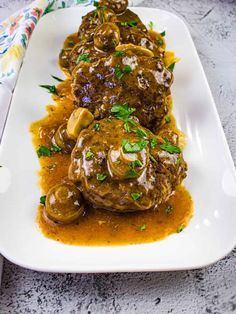 meatballs covered in gravy and garnished with parsley on a white plate