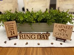 two wooden signs sitting on top of a table next to a planter filled with flowers