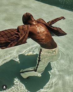 a man is floating in the water wearing white pants and a brown shirt with his arms spread out