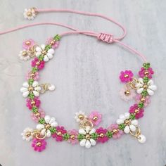 a pink and green beaded bracelet on a marble surface with gold accents, beads and flowers