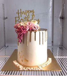 a birthday cake with pink and white flowers on top is sitting in a freezer