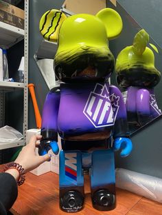 a person holding up a purple and green bear toy on top of a wooden table