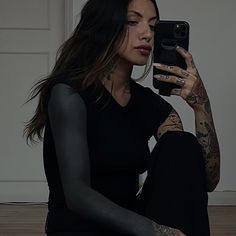 a woman sitting on the floor taking a selfie with her cell phone and tattoos