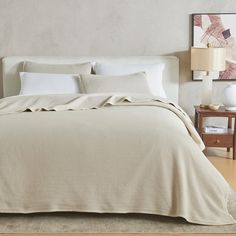 a bed with white sheets and pillows in a room next to a painting on the wall