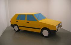 a paper model of a yellow car in a white walled room with grey flooring