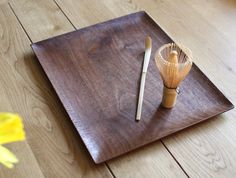 a wooden tray with a whisk on it and a yellow flower next to it